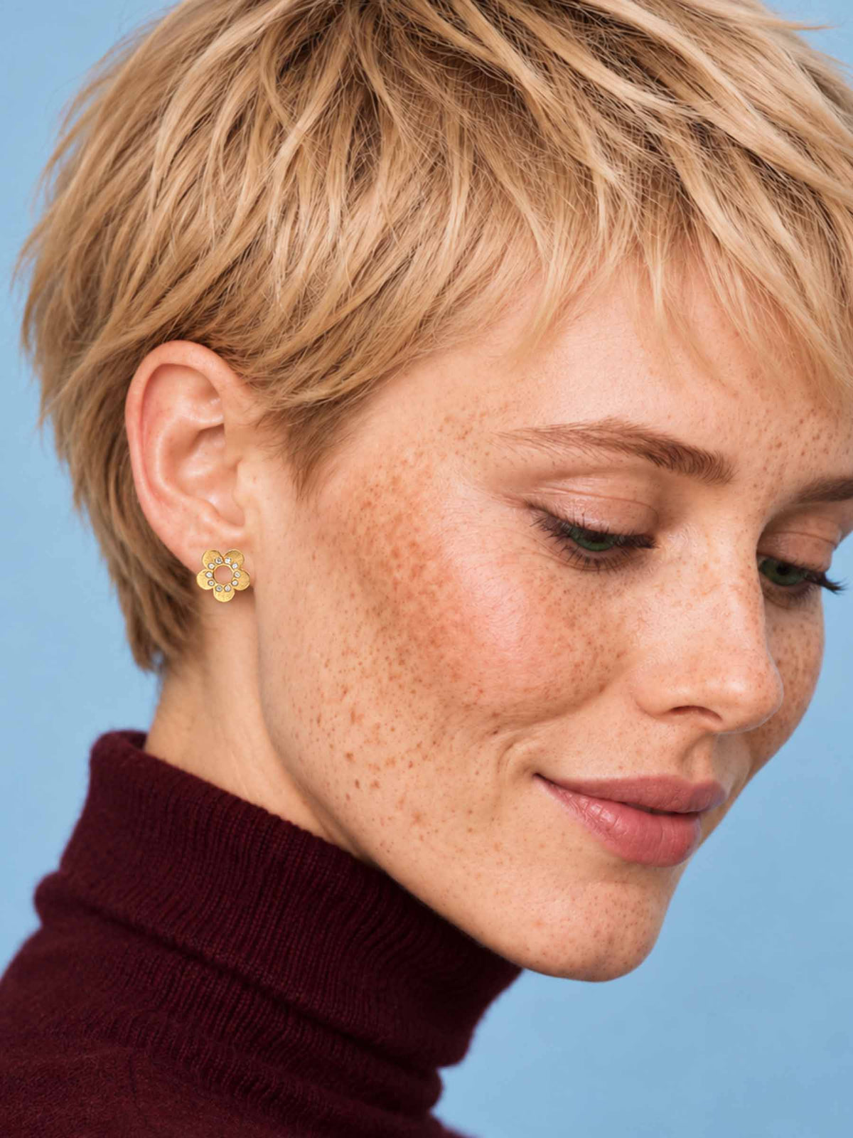 A gold flower-shaped stud earring with five textured petals and small diamonds arranged in a circle around the center, shown on a plain white background.