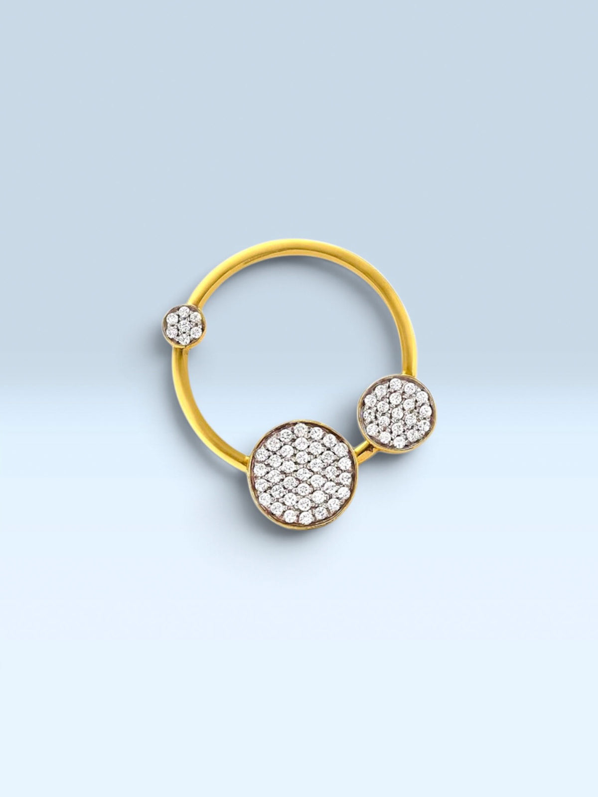 A gold ring featuring three circular pavé-set crystal clusters in different sizes, displayed on a light blue gradient background.